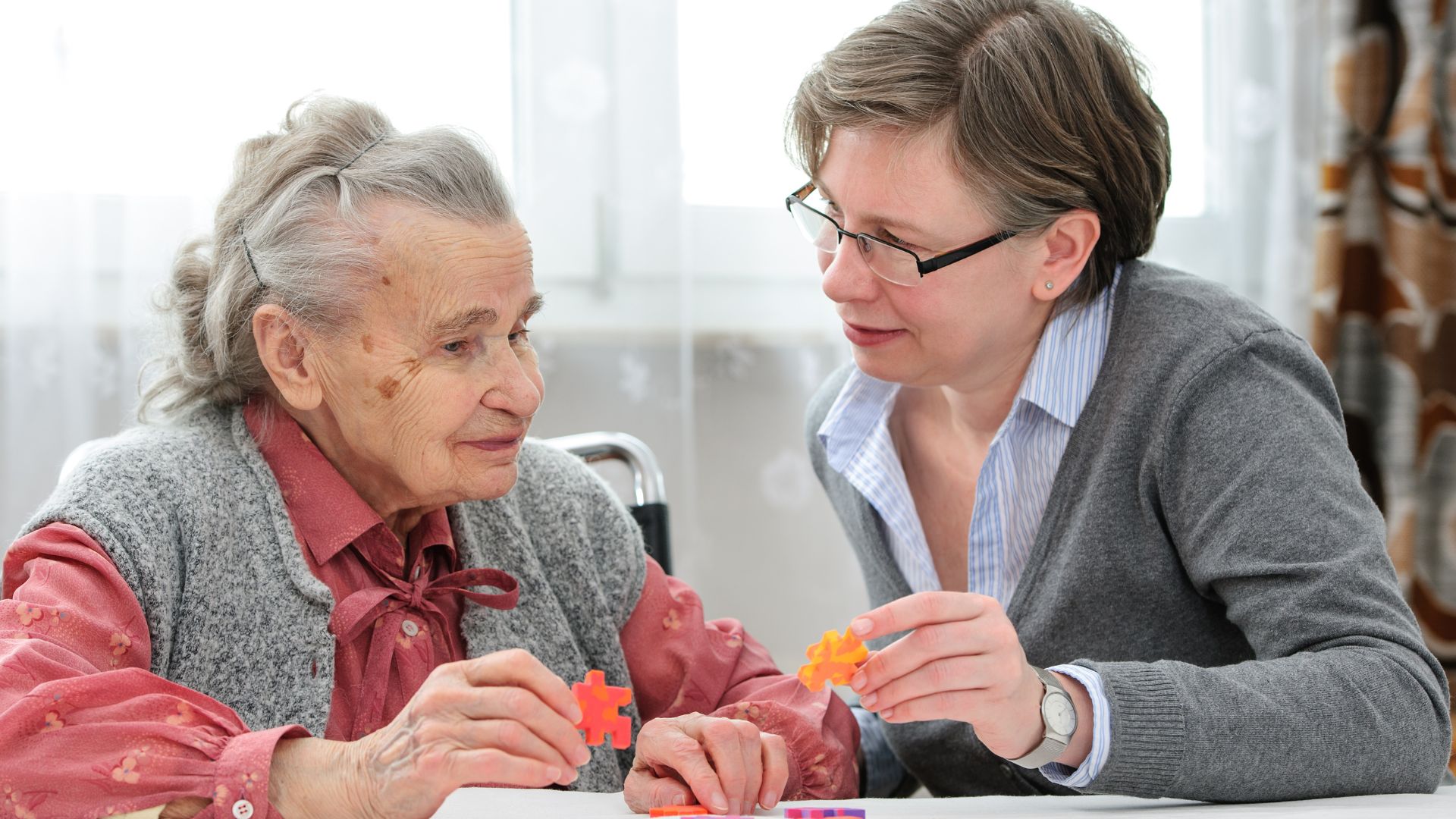 Caregiver engaging an elderly woman in a puzzle activity, fostering connection and mental stimulation in a supportive memory care setting.