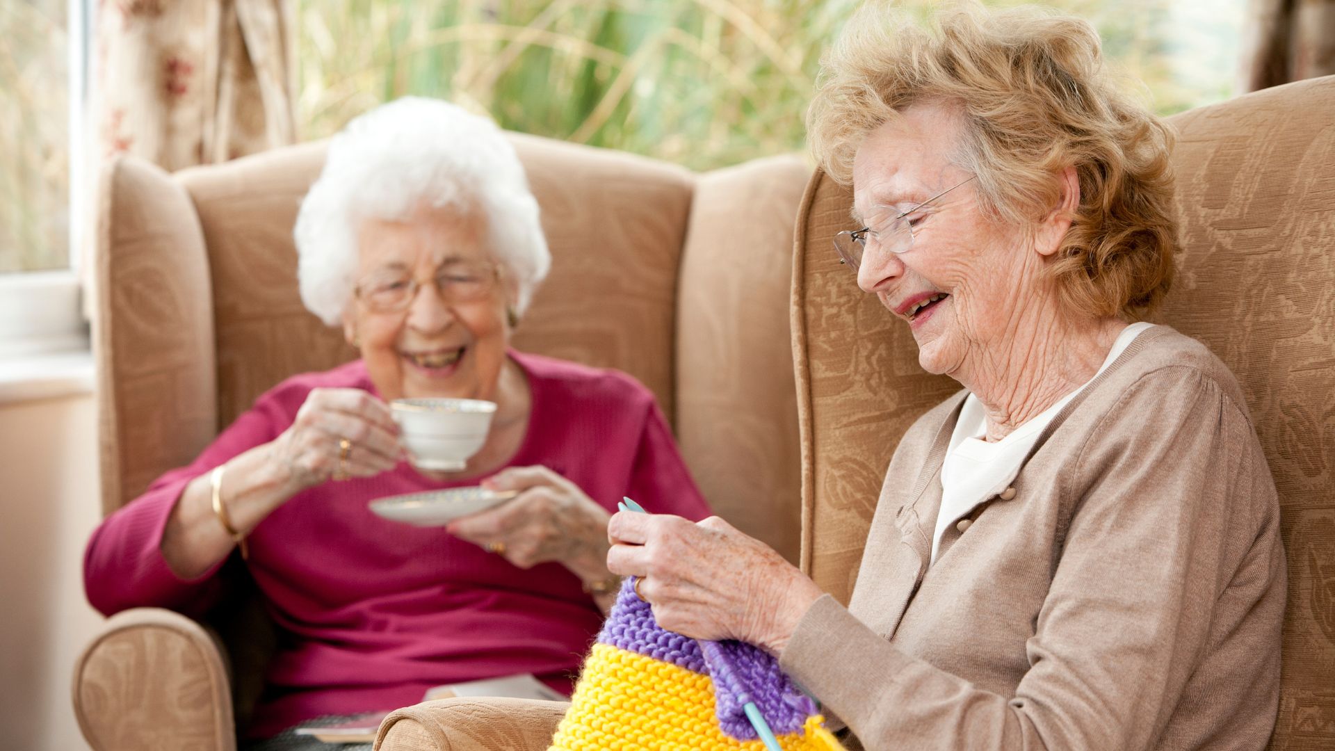 Two senior women enjoying tea and knitting together in a warm, welcoming Independent Living community.