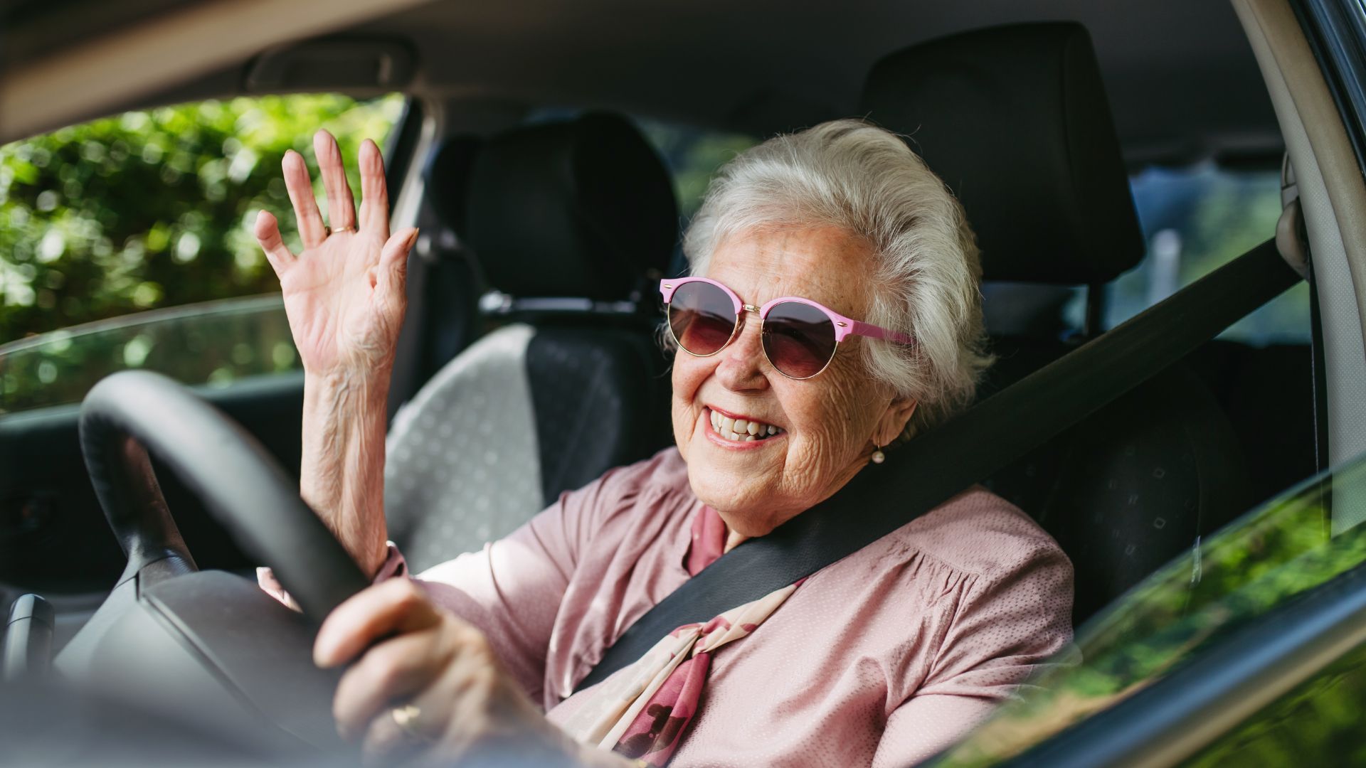 Smiling senior woman behind the wheel, symbolizing independence and the importance of programs that go beyond driving with dignity.”